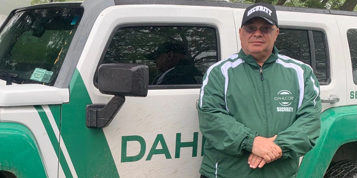 Security guard in green jacket stands by a Dahcore vehicle.