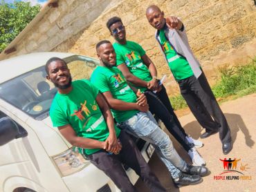 Four men wearing green t-shirts stand in front of a white van.