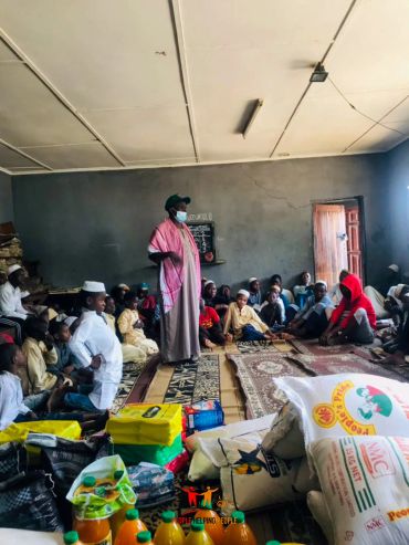 Community gathering with food supplies and a person addressing the group.