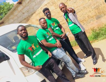 Four men in green 'People Helping People' shirts stand by a white vehicle.