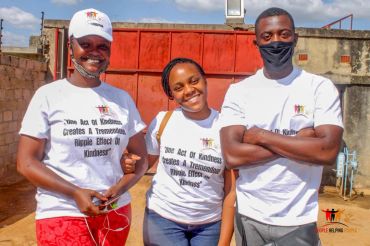 Three people smiling outdoors wearing matching white t-shirts.