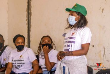 Women in masks and white shirts sitting and standing indoors.