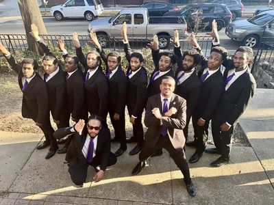 A group of men in suits posing with raised hands outside.