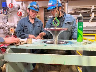 Two workers in blue helmets inspecting industrial equipment.
