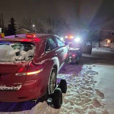 Toyota Venza being towed by a wheel-lift tow truck at night in snowy conditions.
