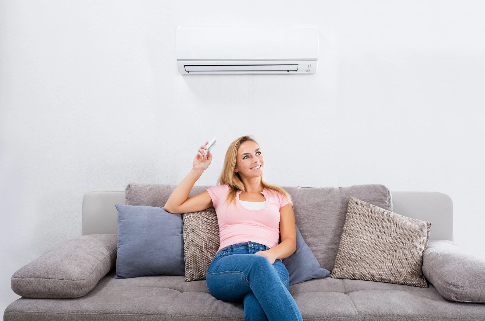 Happy woman sitting on couch with air conditioner remote.