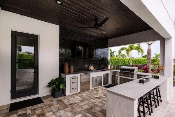 Modern outdoor kitchen with sleek appliances and bar seating under a dark wood ceiling.