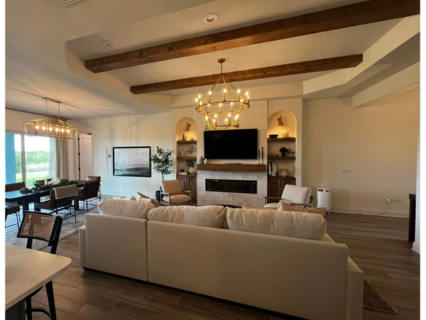 Modern living room with beige sofa, wooden beams, and elegant chandeliers.