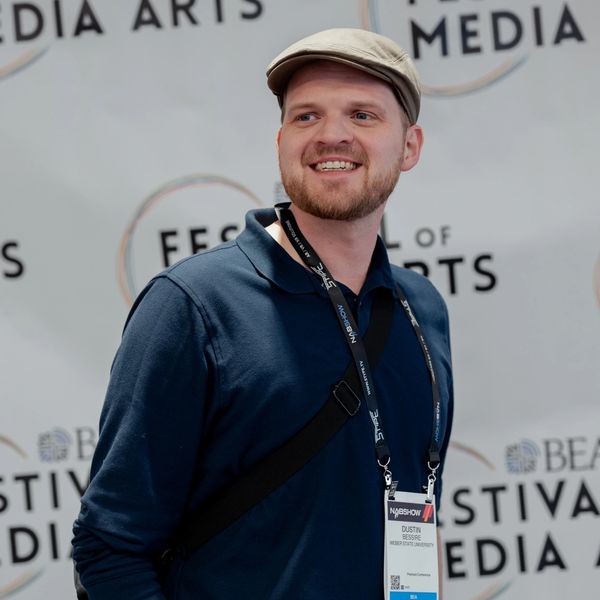 Man wearing a cap and badge at a media arts festival.