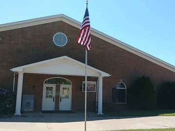 A brick building with a white porch and an American flag in front.