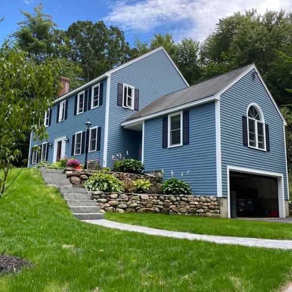 Blue two-story house with black shutters and a stone retaining wall.