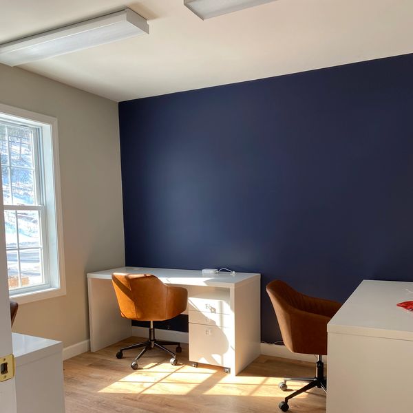 Bright office with white desks, brown swivel chairs, and a deep blue accent wall.