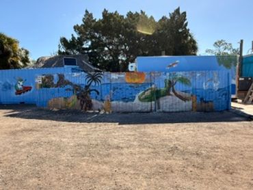 Colorful mural depicting a tropical beach scene on a curved wall under bright sunlight.