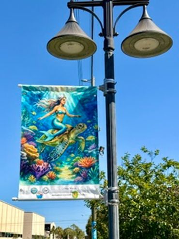 Colorful banner of a mermaid riding a sea turtle on a street lamp.