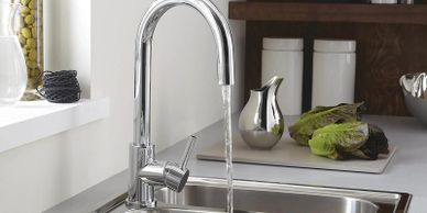 Modern chrome kitchen faucet with running water over a stainless steel sink.
