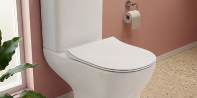 Modern white toilet in a pink bathroom with a toilet paper roll.