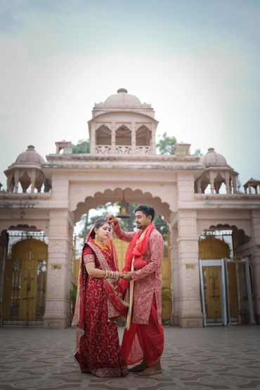Indian couple in traditional wedding attire under a historic archway.