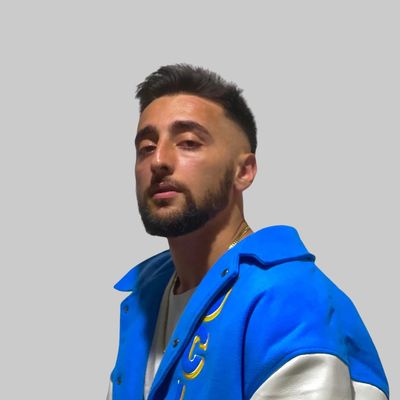 Man with a beard and short hair wearing a blue varsity jacket.