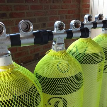 Row of yellow scuba tanks with protective netting lined up indoors.