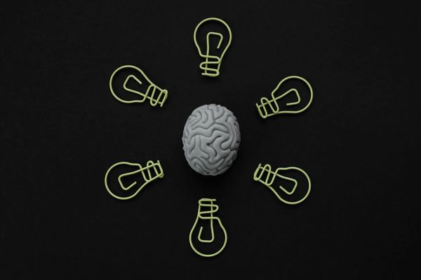 A brain surrounded by six wireframe light bulbs on black background.