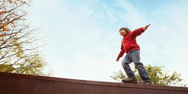 Child balancing on a wooden beam outdoors.