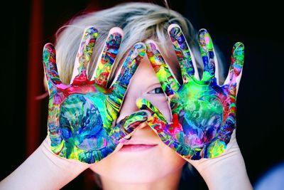 Child shows hands covered in vibrant multicolored paint.