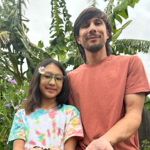 A man and a girl smiling outdoors with plants in the background.