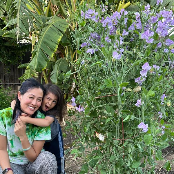 A woman and child smiling in a garden with tall flowering plants.