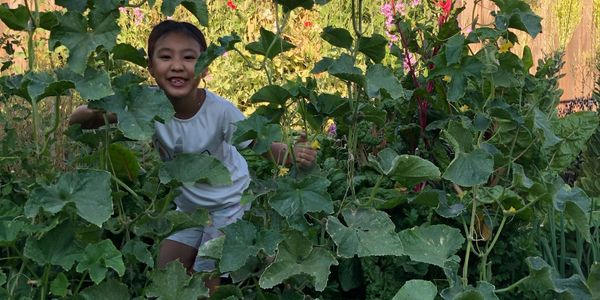 Child smiling and playing in a lush garden with tall green plants.