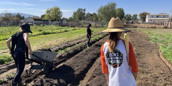 Three people working on a farm field under a clear sky.