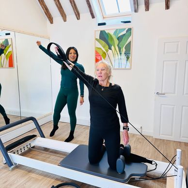 1:1 Session Pilates reformer with a trainer guiding her.