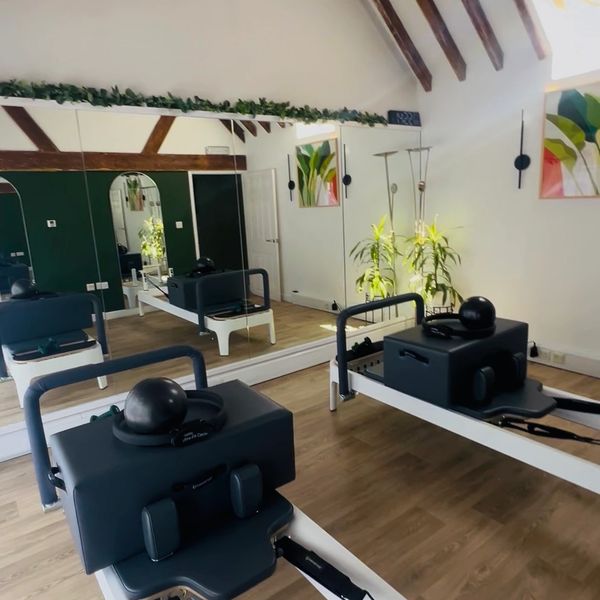 Modern Pilates studio with reformer machines and wooden beams.