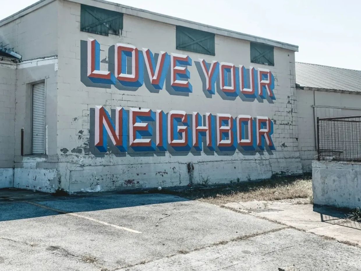 Bold mural on wall says 'LOVE YOUR NEIGHBOR' in 3D letters.