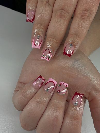 Pink and red heart-themed nail art with rhinestones on square nails.