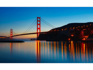 Golden Gate Bridge illuminated at dusk with water reflections.