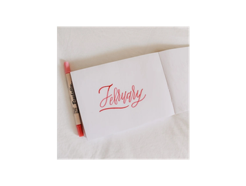 A notebook opened to a page with "February" written in red calligraphy and a red marker beside it.