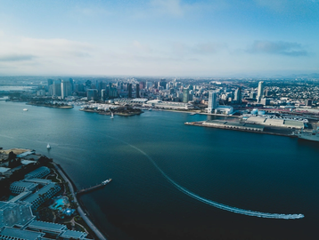 A city skyline across a wide river with boats and clear blue sky.