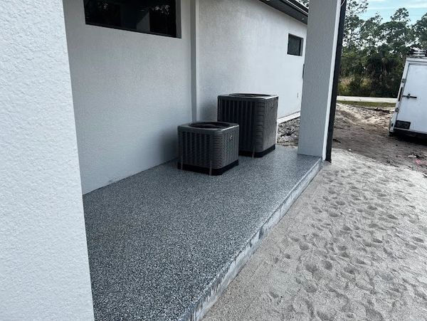 Two air conditioning units on a speckled concrete platform outside a building.