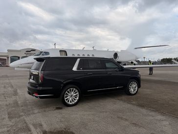 Black Cadillac Escalade chauffeur vehicle parked on an airport tarmac beside a private jet, represen
