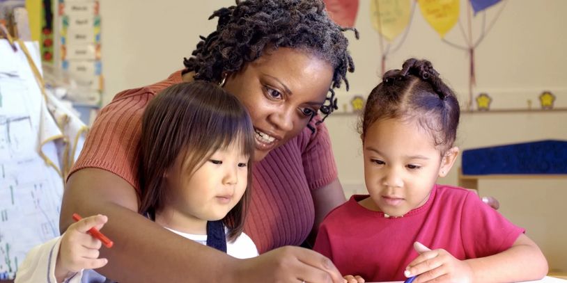 Teacher helping two young girls with drawing in a classroom.
