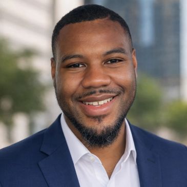 Smiling man in a blue suit jacket outdoors.