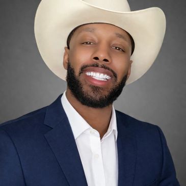 Man smiling in a cowboy hat and blazer.