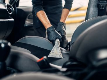Person cleaning car seat upholstery with a vacuum extractor tool.