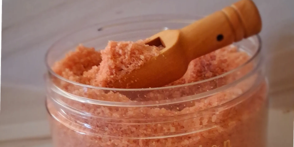 Pink bath salt with wooden scoop in a clear jar.