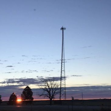 Sunset with a tall communication tower and trees.