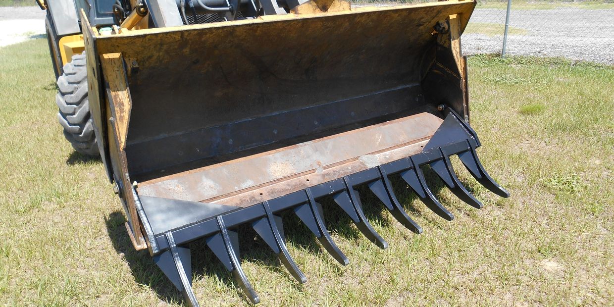 Close-up of a large loader bucket attachment with black metal teeth on a backhoe.