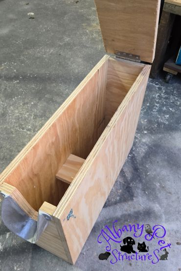 Open wooden box with a hinged lid on a concrete floor.