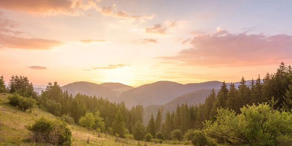 A beautiful outdoor landscape with sun illuminating light clouds from behind distant mountains.