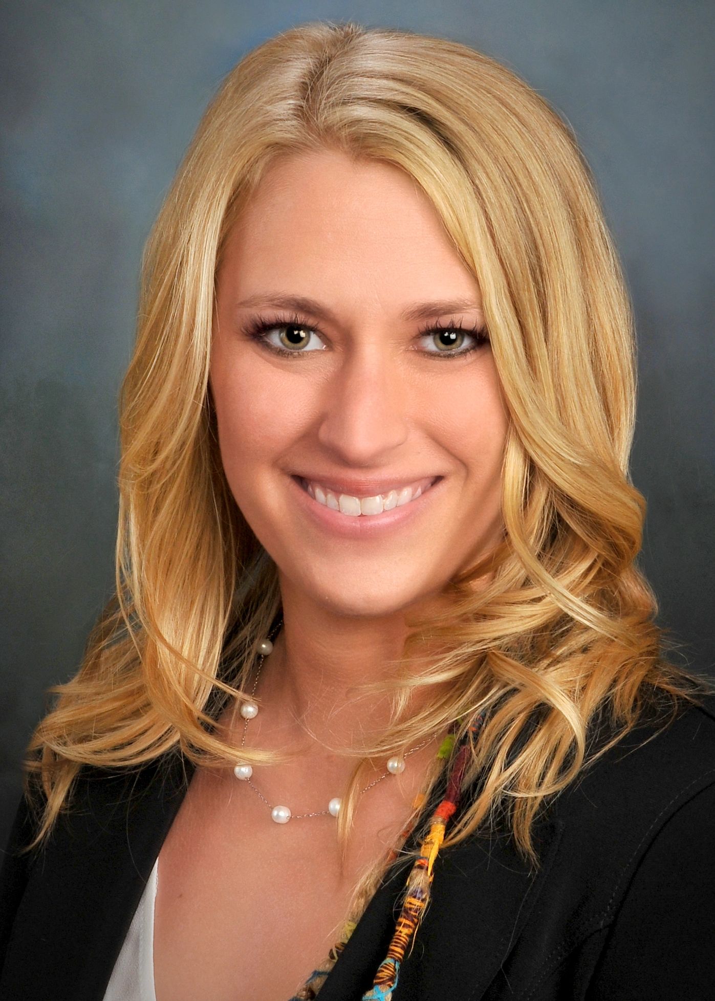 Professional headshot of a smiling blonde woman, with pearl necklace.