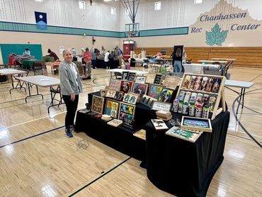 Woman stands beside a display of dog-themed art and products at a community center event.